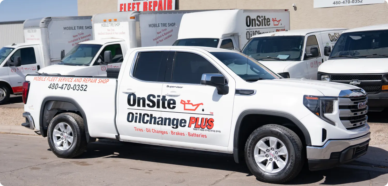 A white pickup truck with OnSite OilChange PLUS and contact details printed on the side is parked in front of a fleet repair shop, showcasing mobile auto repair services alongside several branded service vans in the background.