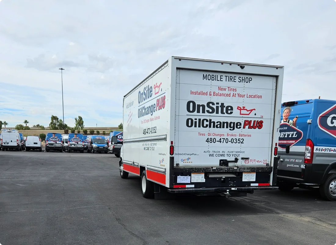 A white box truck labeled OnSite OilChange Plus is parked in a lot among other service vans. The truck advertises mobile tire and oil change services with a contact number and website for convenient onsite maintenance.