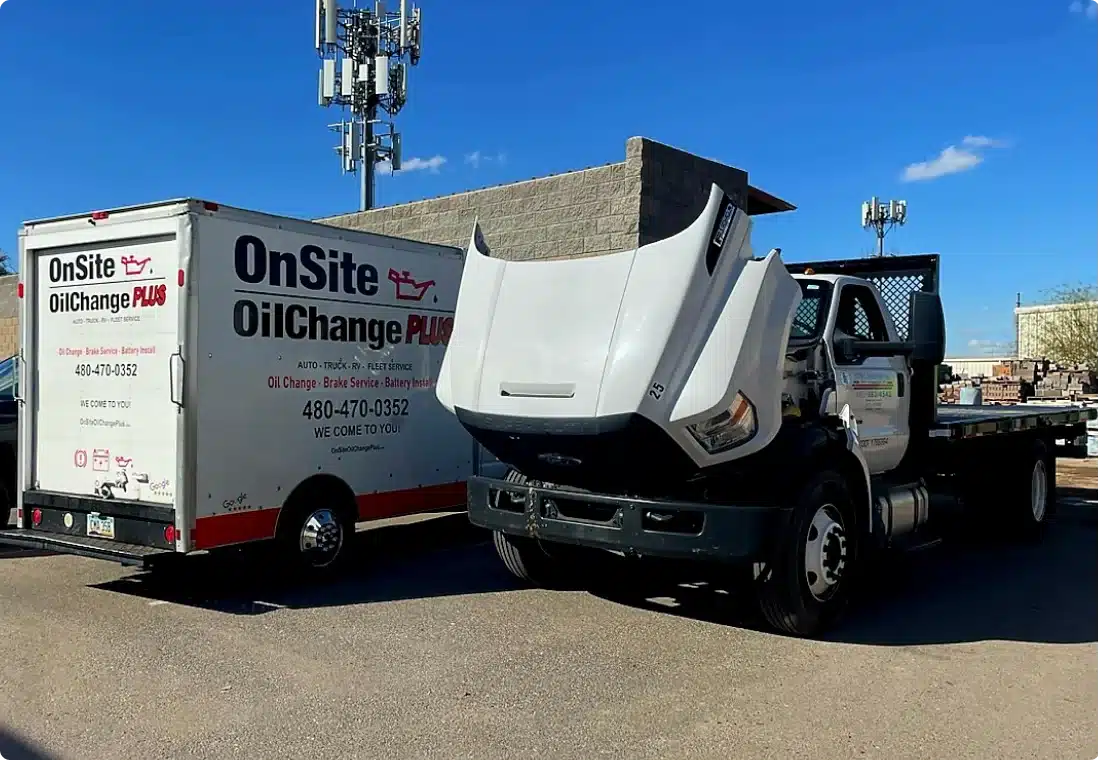 A white OnSite Oil Change Plus service truck with its hood open is parked next to a branded white box van in a parking lot, ready to provide convenient oil change services under a clear blue sky.